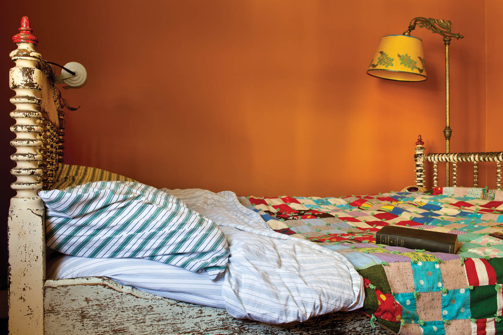 Photo of a wooden bedframe with bright patchwork blanket.