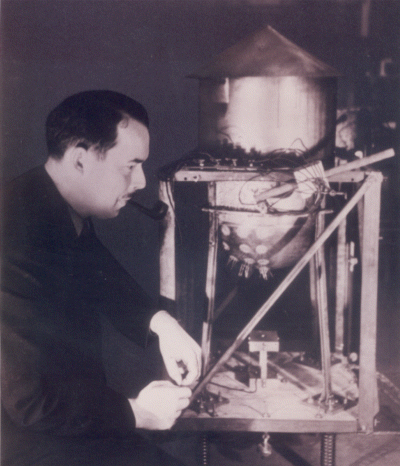 Photograph depicting A.C. Ruge carrying out experiments on a small scale model of a water tank fitted with the first strain gages mounted on a vibration table in 1938.