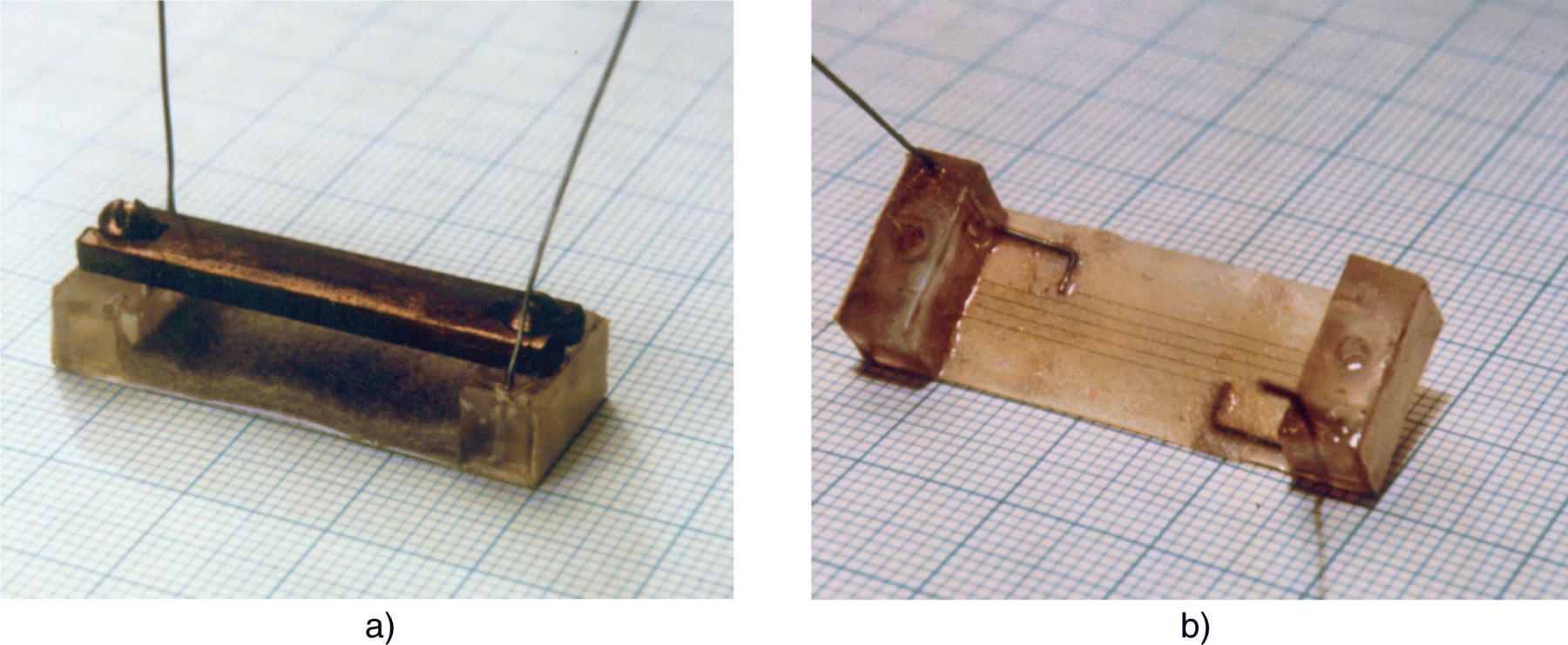 Photographs depicting Ruge's strain gage from 1938 (a) with brass bar as an installation aid and (b) without brass bar and without grid protection layer.