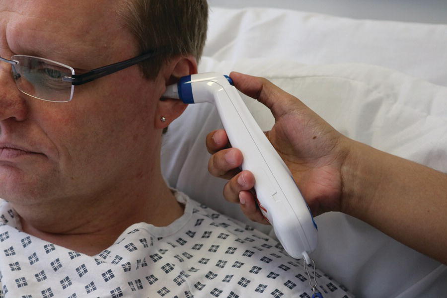 An electronic tympanic thermometer inserted into the left ear of a male patient.