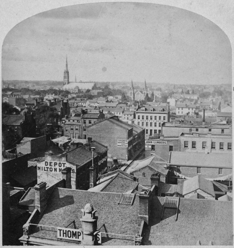 Old black and white photograph of Toronto taken from a rooftop. The horizon is in view with a church steeple in the distance.